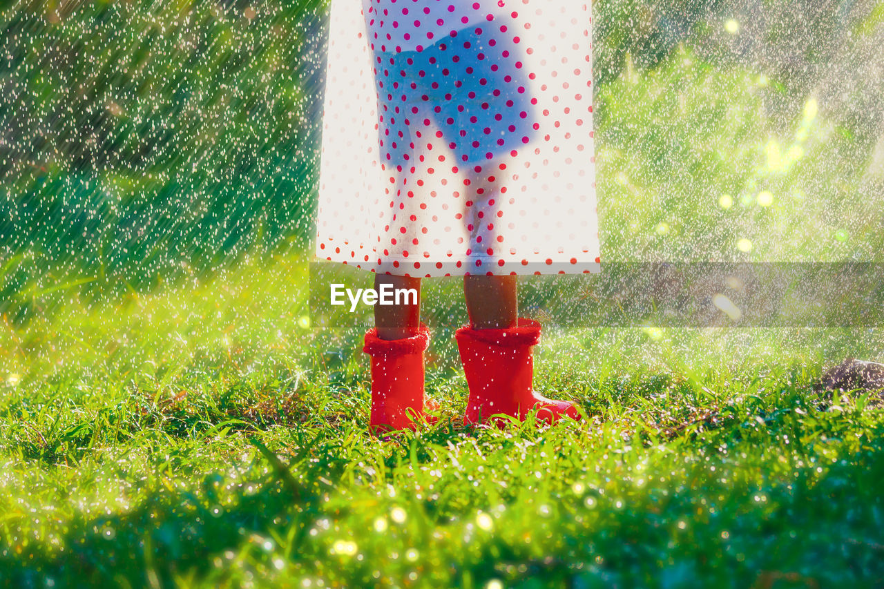 Low section of person wearing rubber boots and raincoat while standing on grass during rainfall