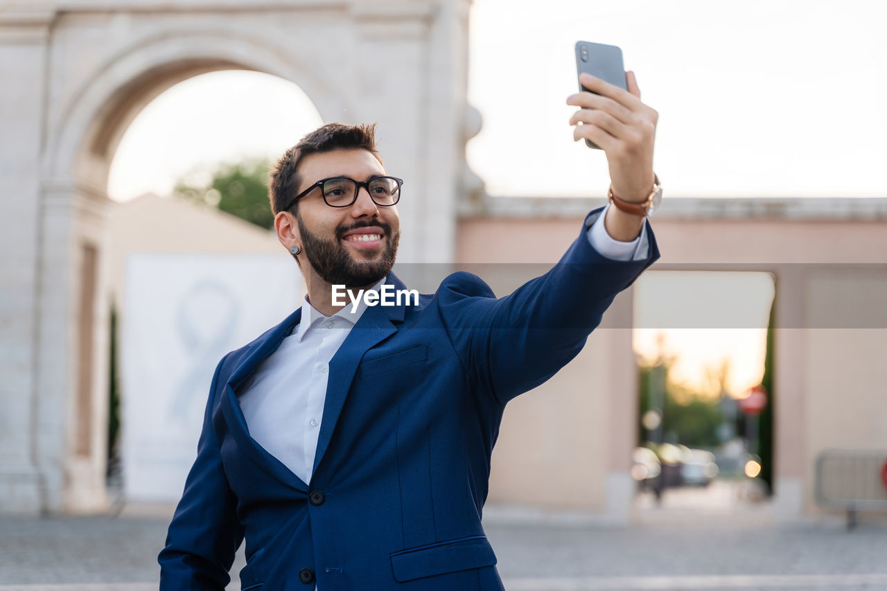 A young man in a suit using mobile phone and taking selfie