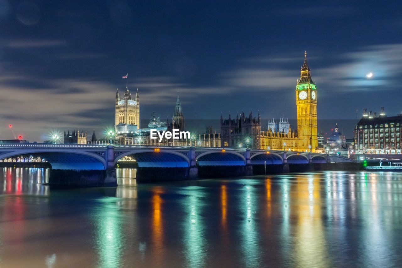 Westminster bridge over thames river by illuminated big ben and city at night