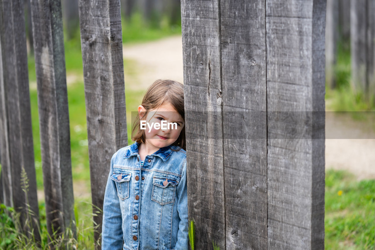 Portrait of smiling girl standing by plank outdoors