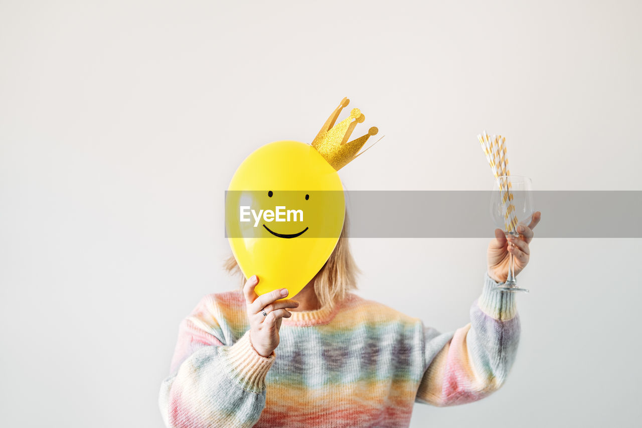 one person, studio shot, yellow, fun, smiling, smiley, humor, indoors, happiness, front view, cartoon, holding, adult, copy space, emotion, waist up, creativity, portrait, anthropomorphic smiley face, cheerful, childhood, white background, obscured face, toy, emoticon, child, women, positive emotion, standing