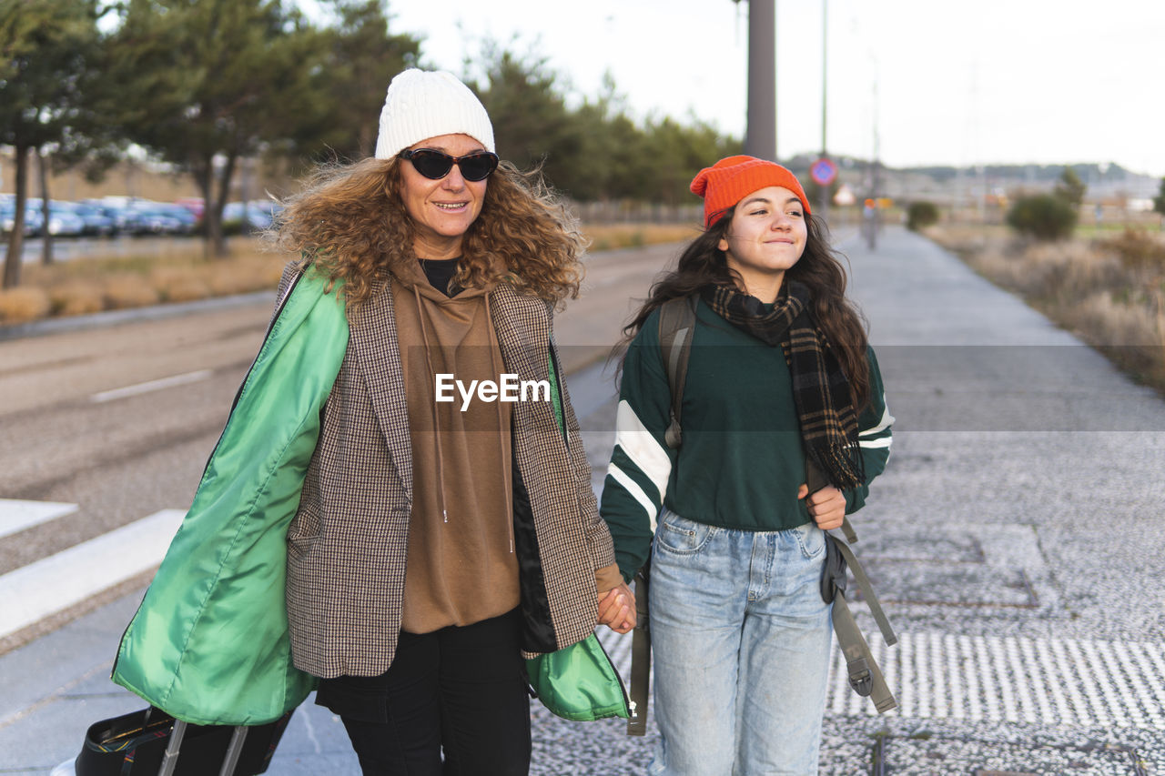 Happy mother and daughter holding hands walking on road