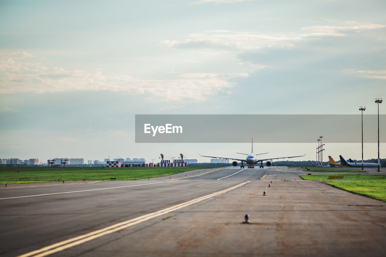 Airplane at airport runway against cloudy sky