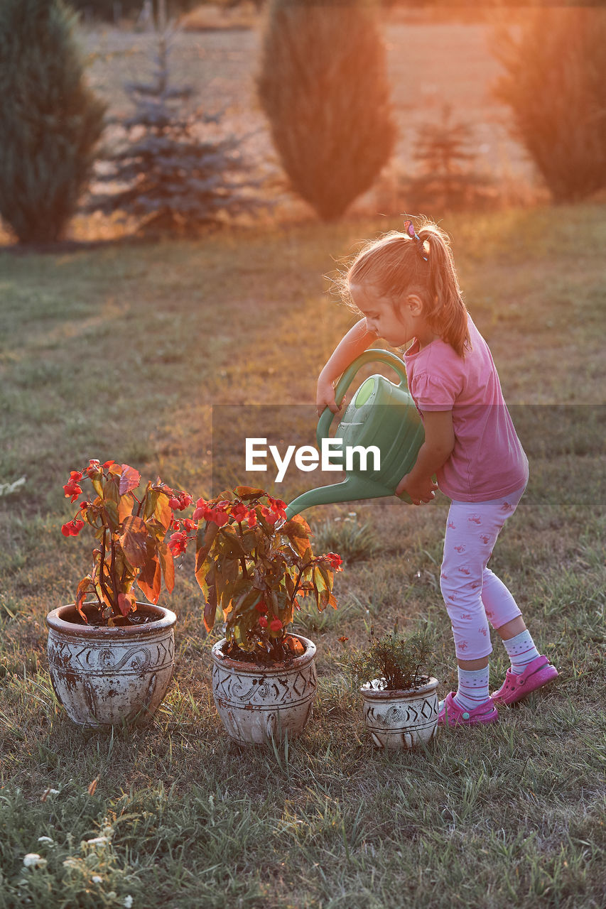 Girl watering plants while standing on grass