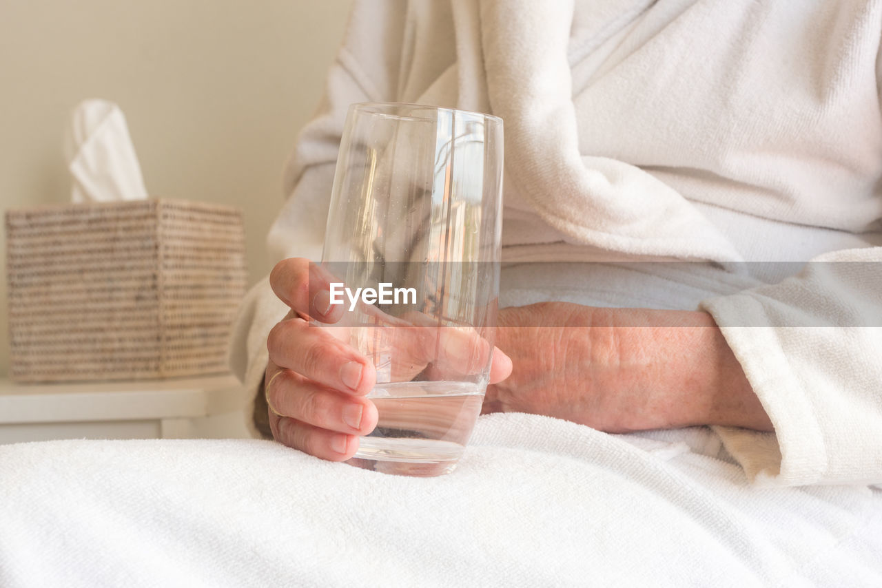 Midsection of woman having drink while sitting on bed