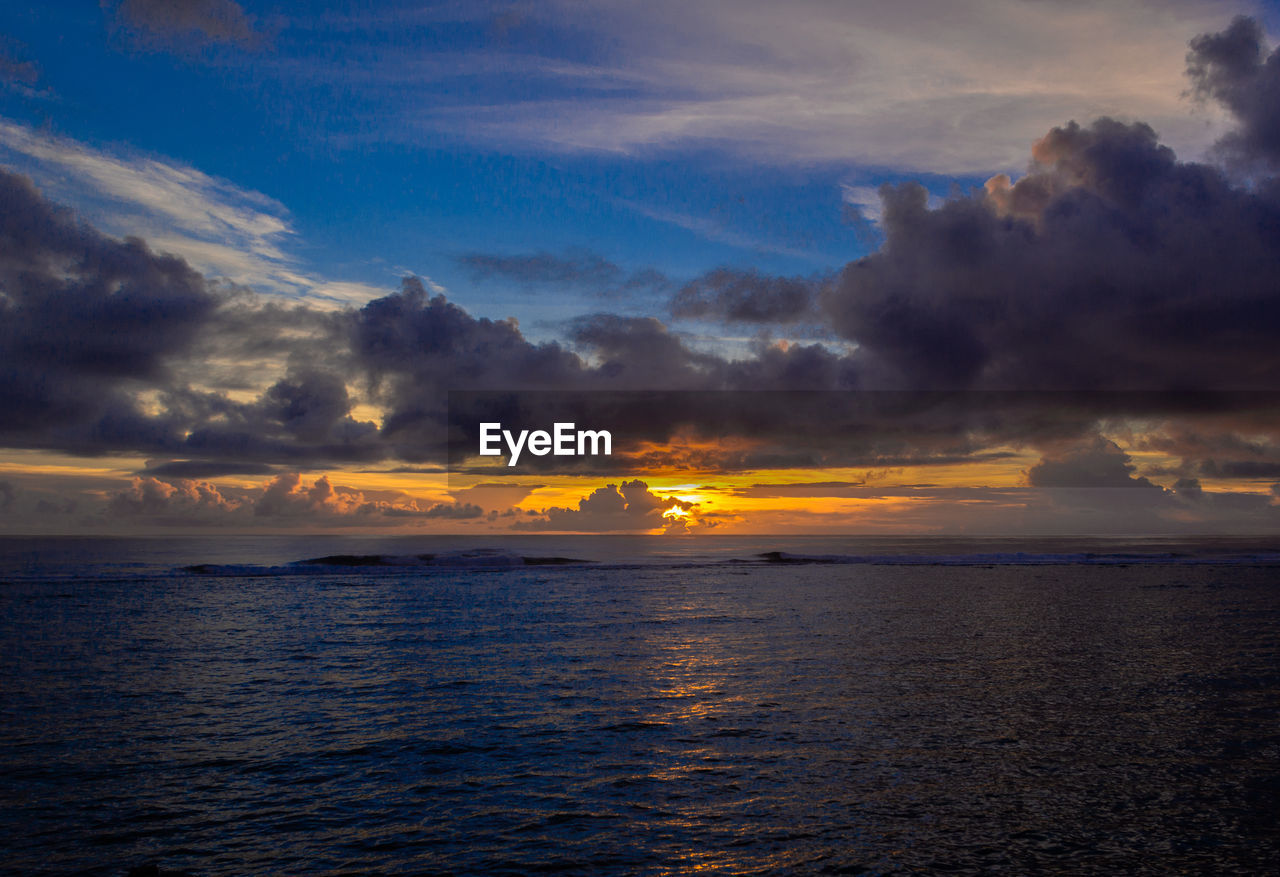 Scenic view of sea against dramatic sky during sunrise