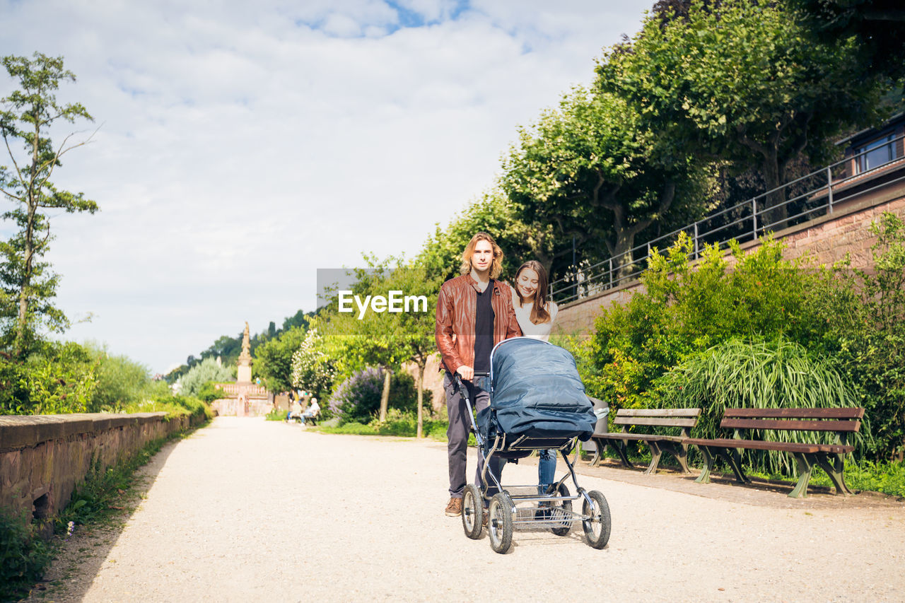 Smiling couple with baby stroller walking in park