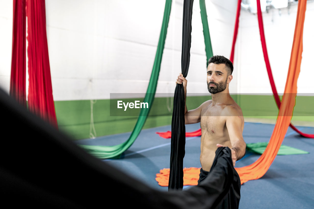 Crop muscular man grasping piece of black aerial silk during dance rehearsal in modern studio