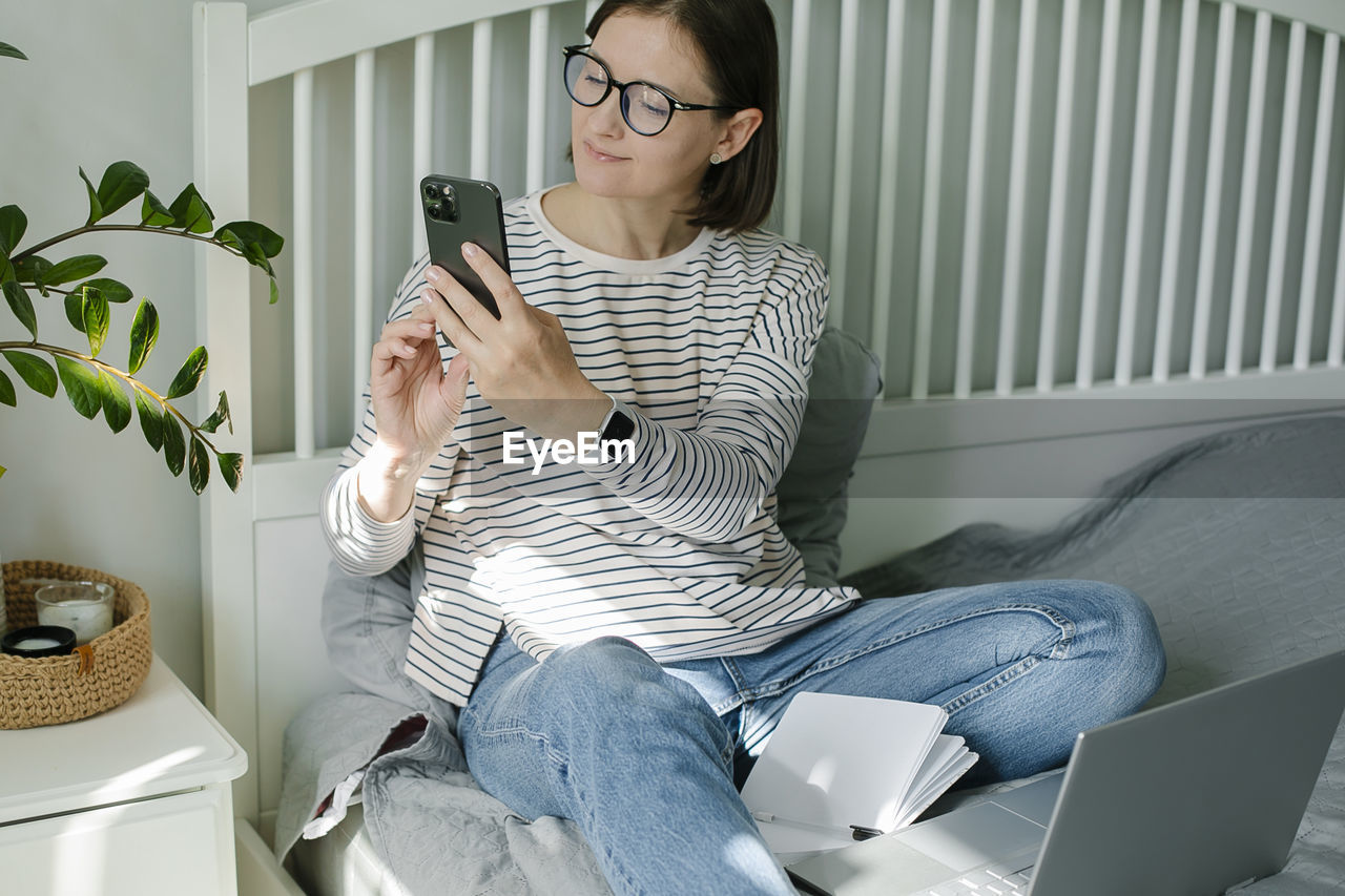 portrait of young woman using phone while sitting on sofa at home