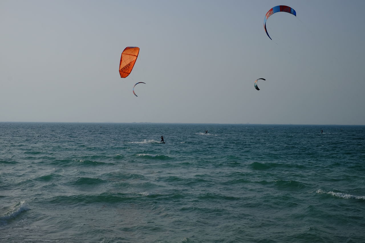 Person paragliding over sea against clear sky