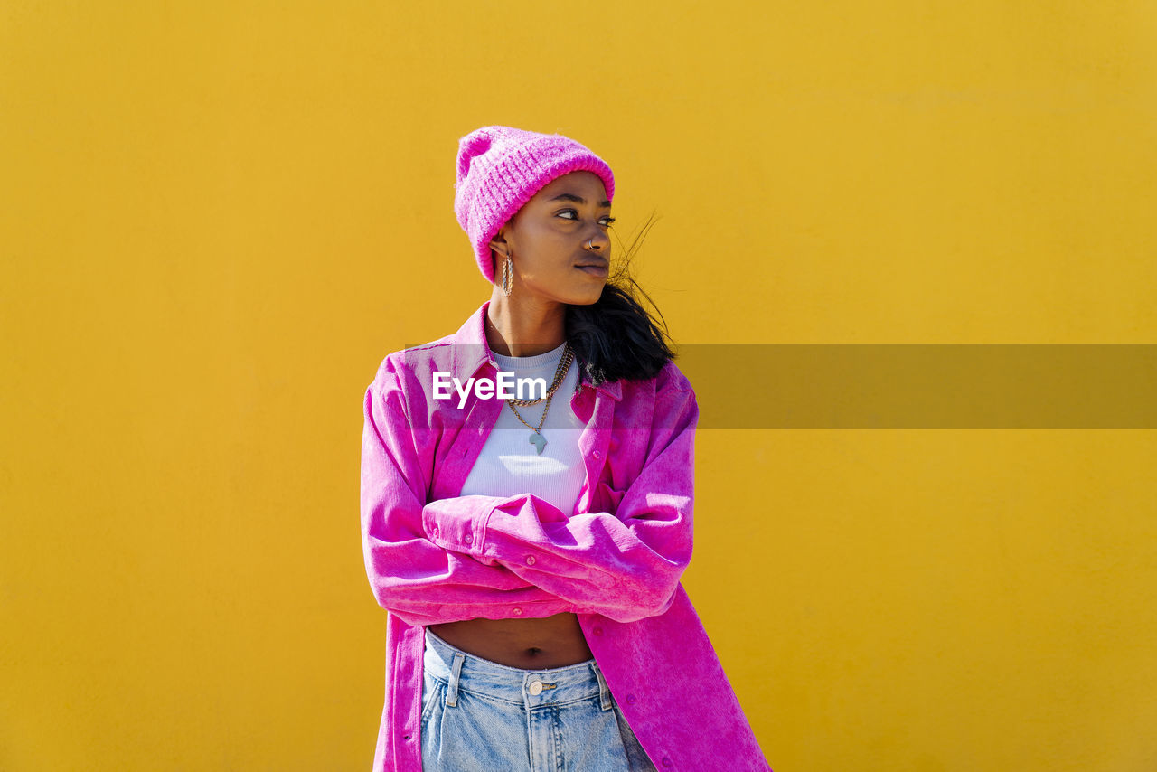 Young woman wearing knit hat standing with arms crossed on sunny day