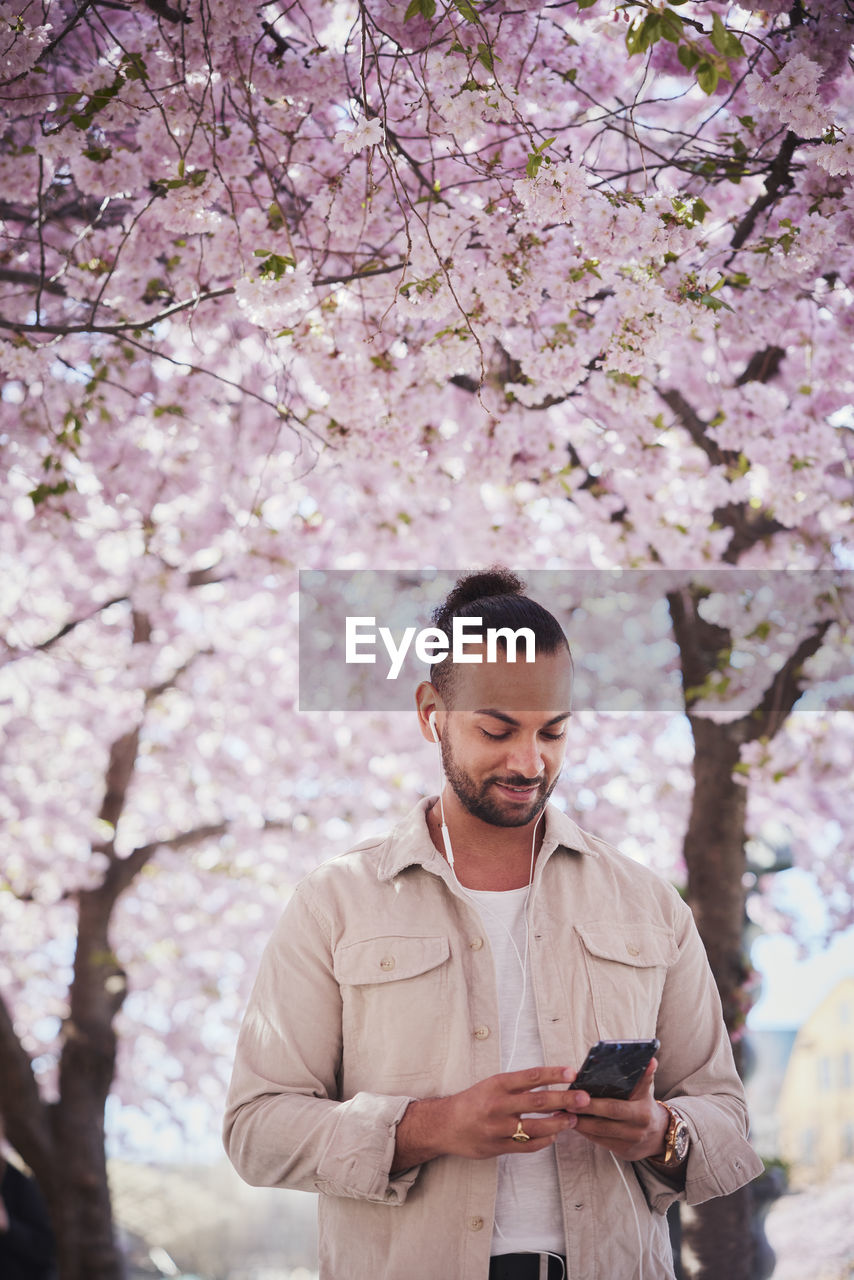 Young man standing under cherry blossom and using phone