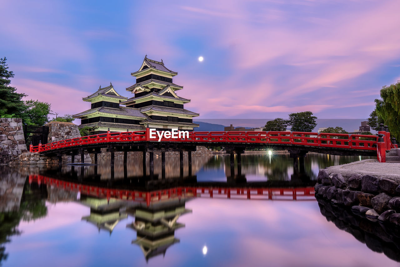 Temple by bridge and river against sky during sunset