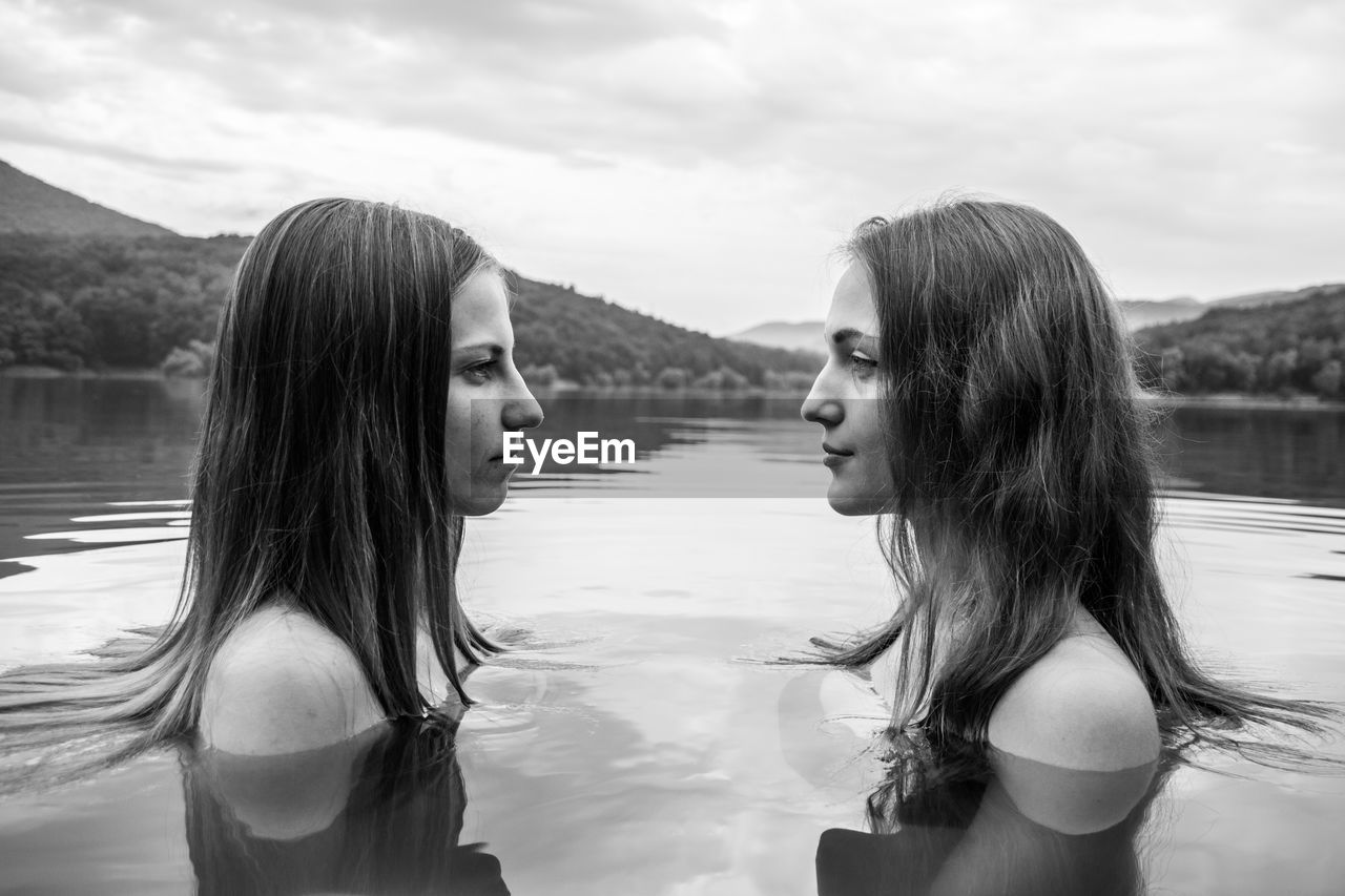 Profile view of shirtless female friends face to face in lake