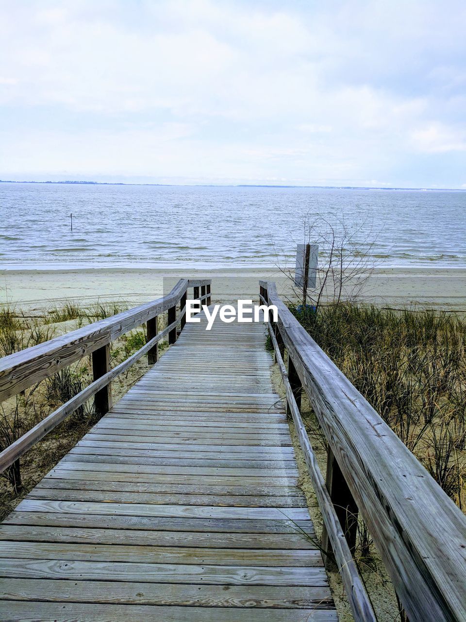 Wooden boardwalk leading towards sea against sky