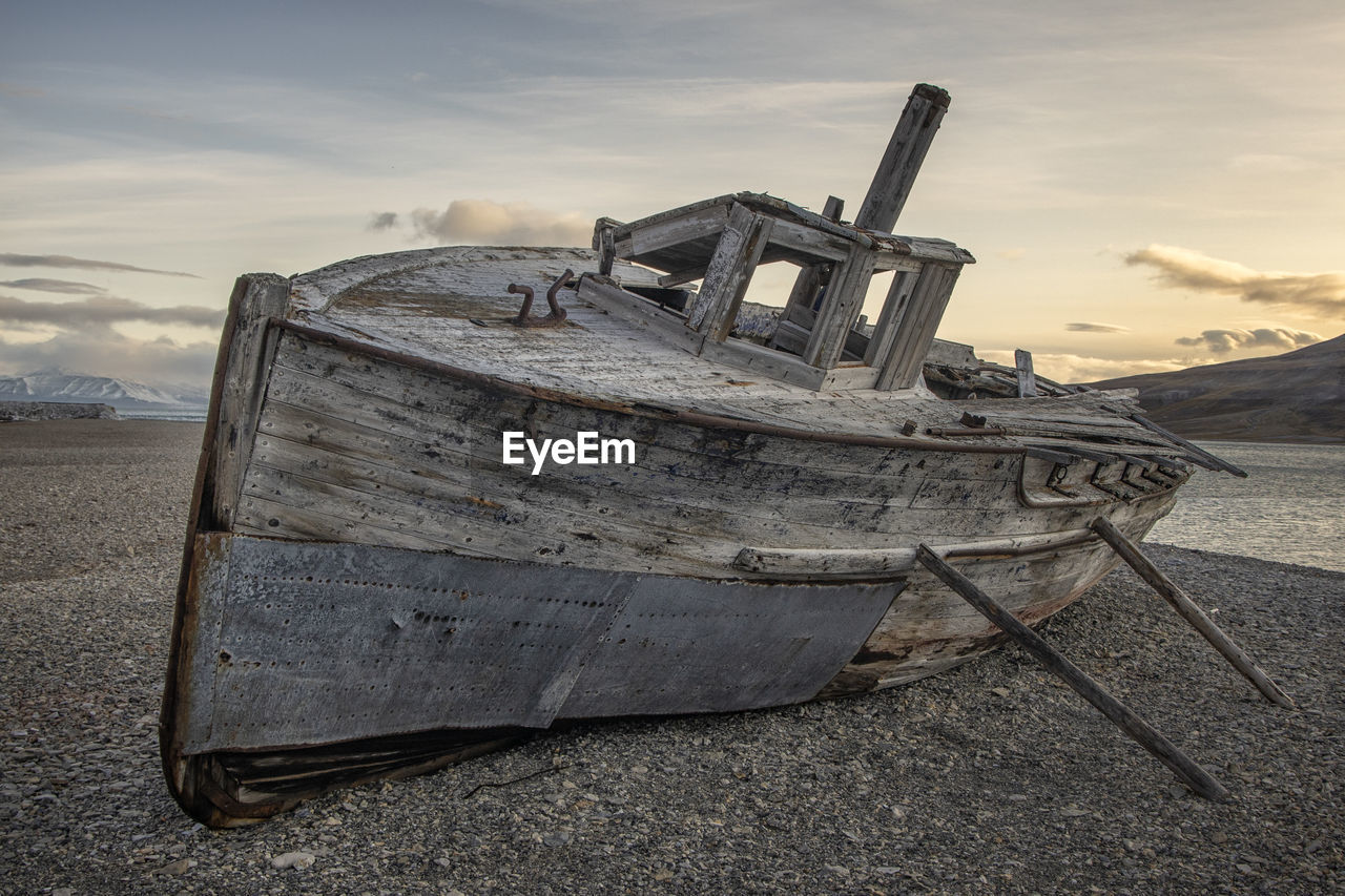 DAMAGED BOAT ON BEACH AGAINST SKY