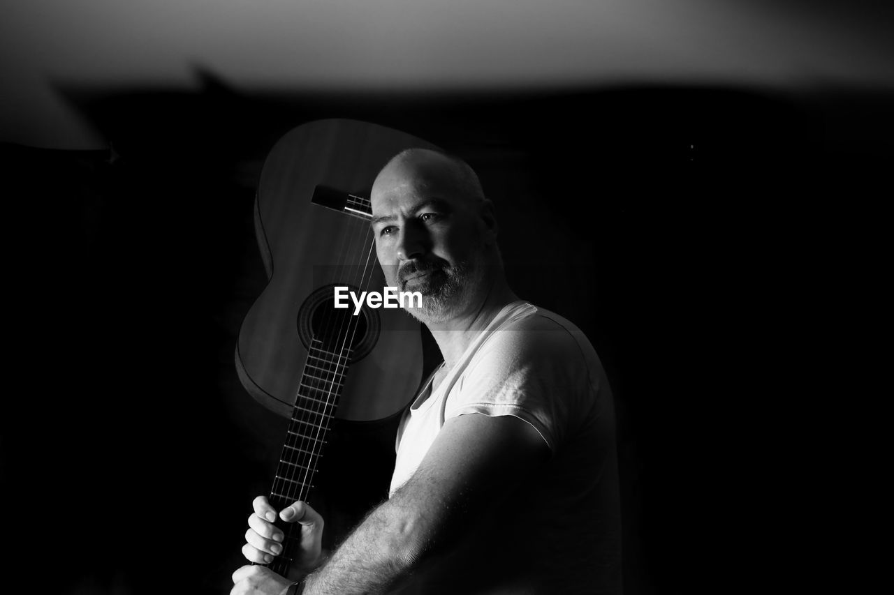 Bald man holding guitar against black background