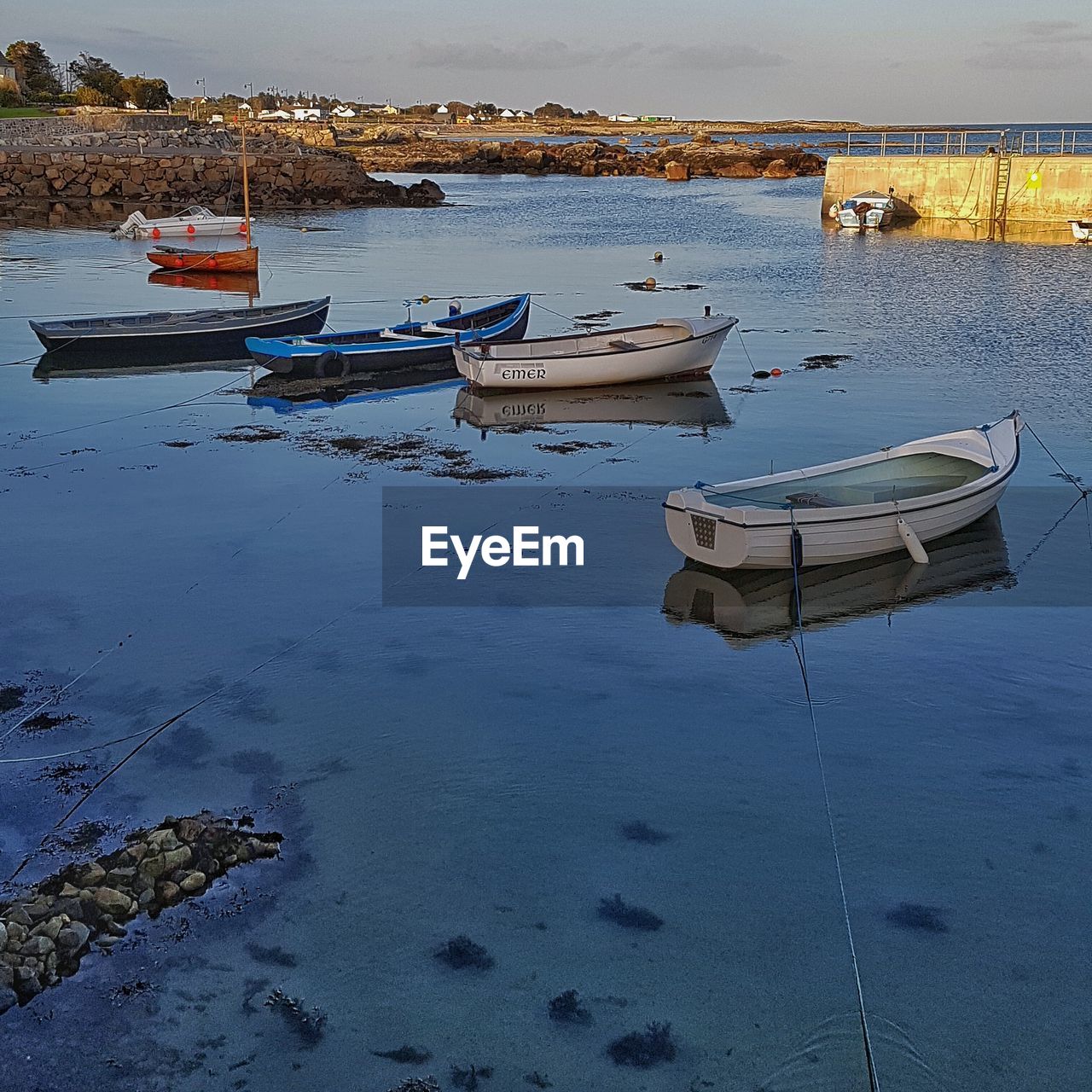 BOATS MOORED IN SEA WITH REFLECTION OF CLOUDS IN BACKGROUND