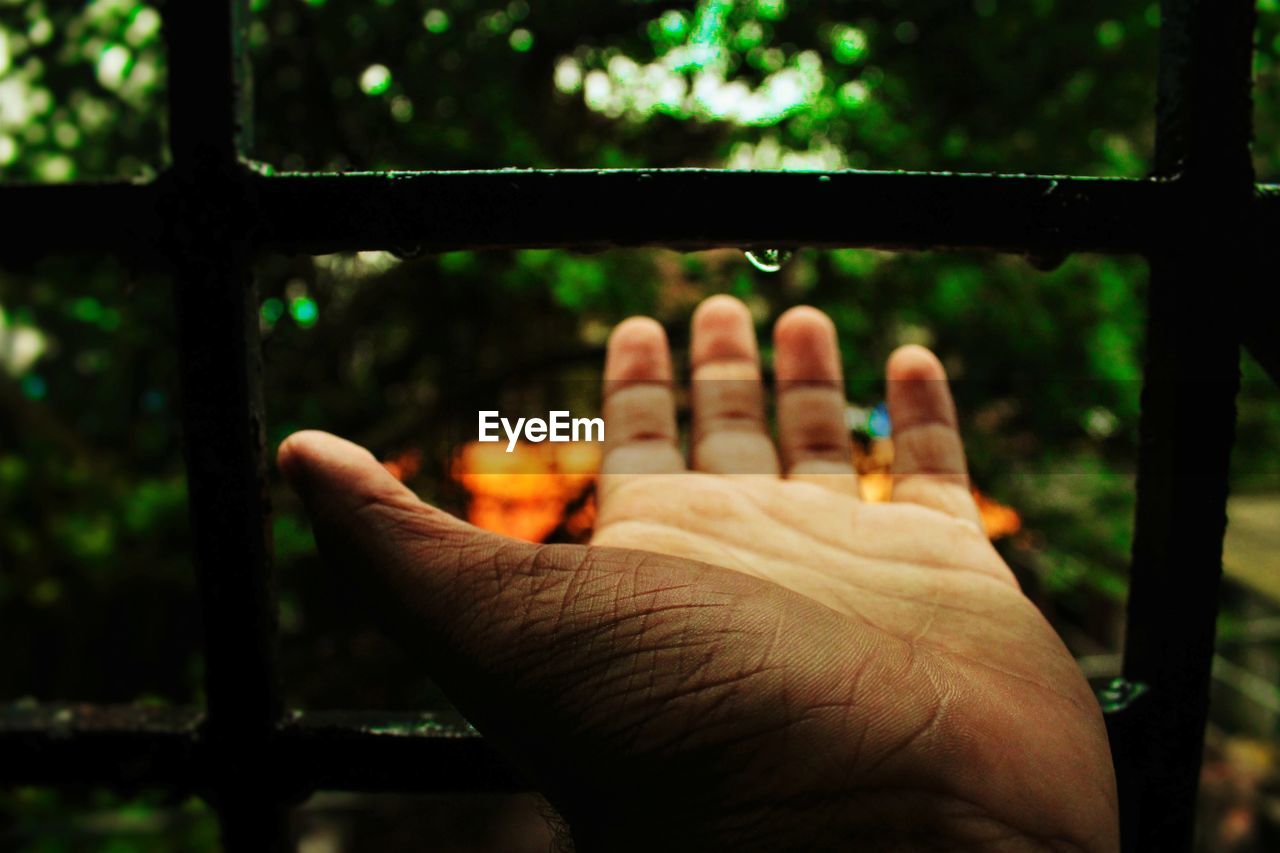 Close-up of hand catching water drop on railing outdoors