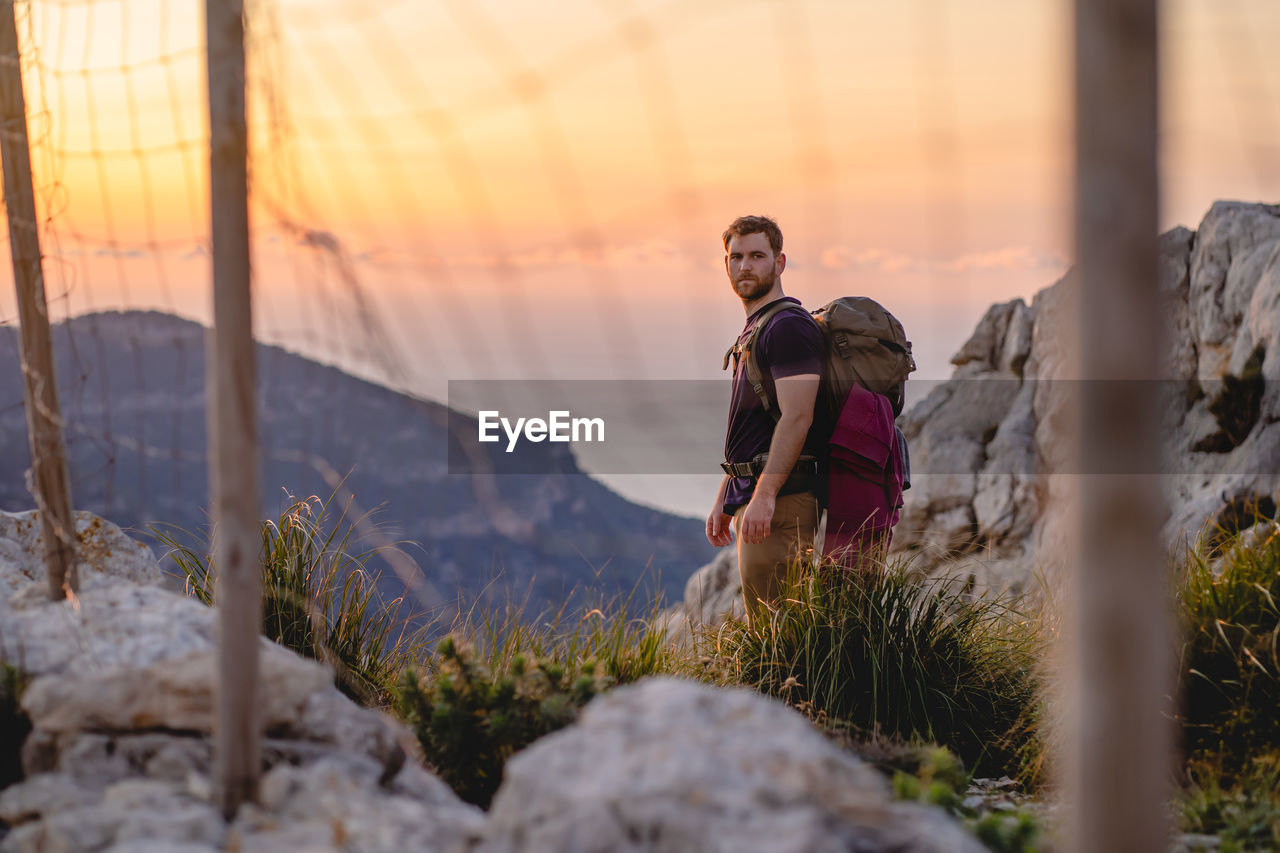 Lonely traveler stands on a viewpoint of a mountain during sunset