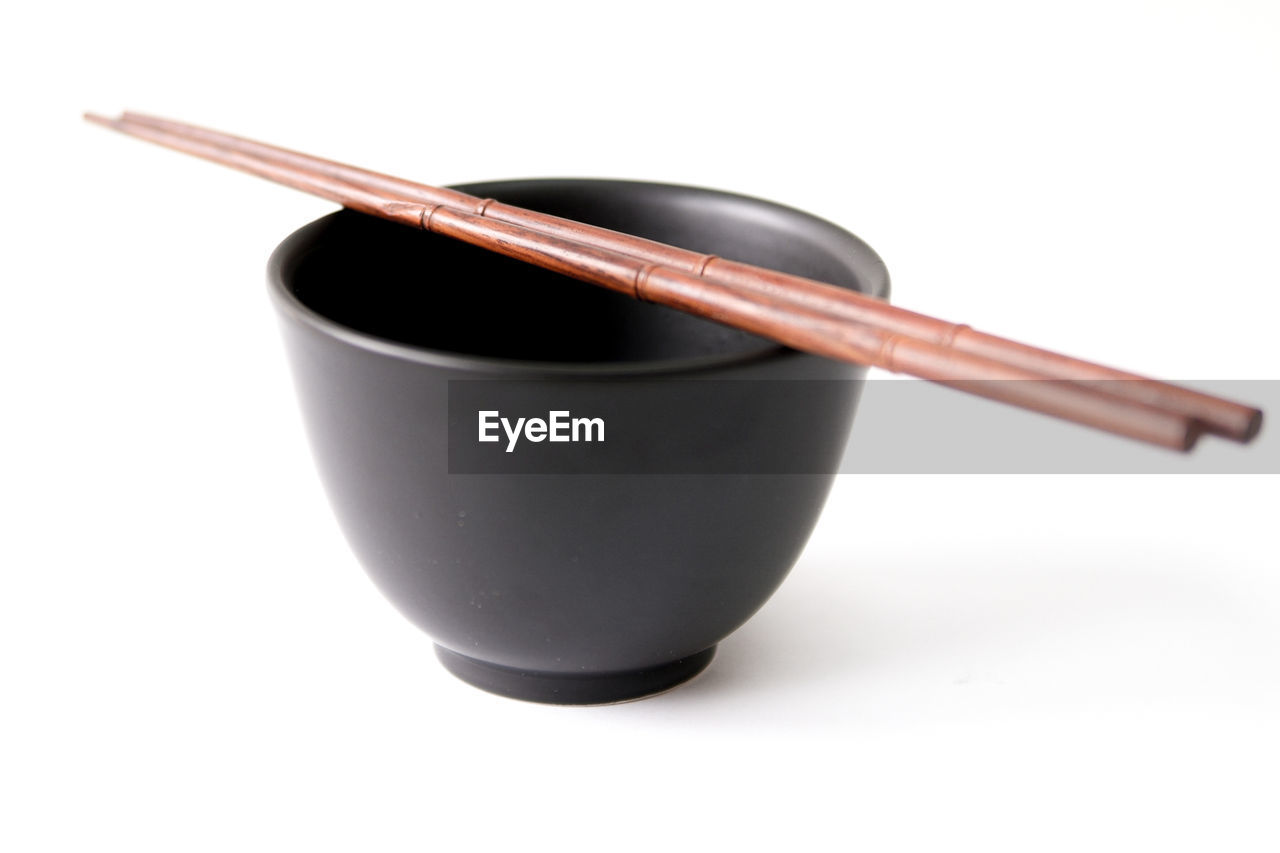 Close-up of empty black bowl with chopsticks against white background