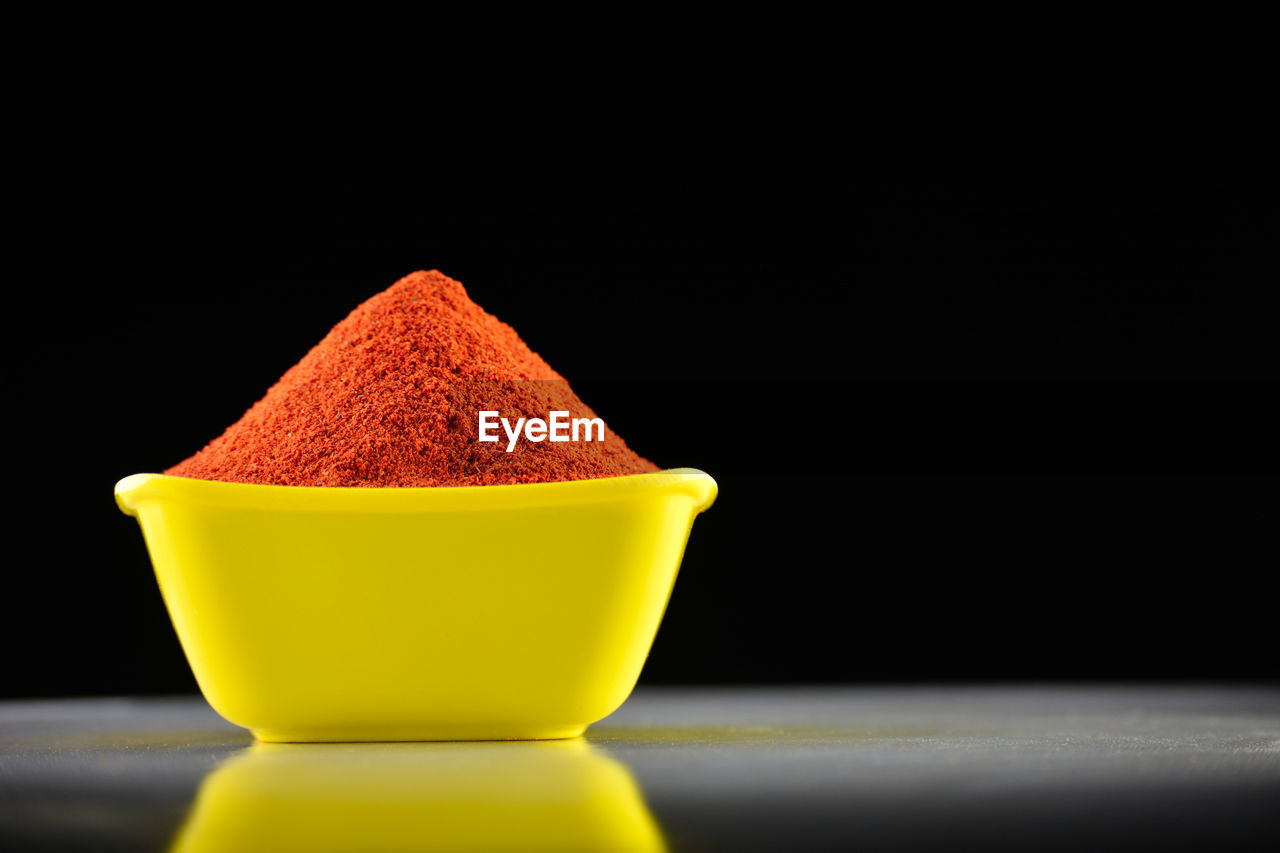 Red chili powder in yellow bowl on dark background