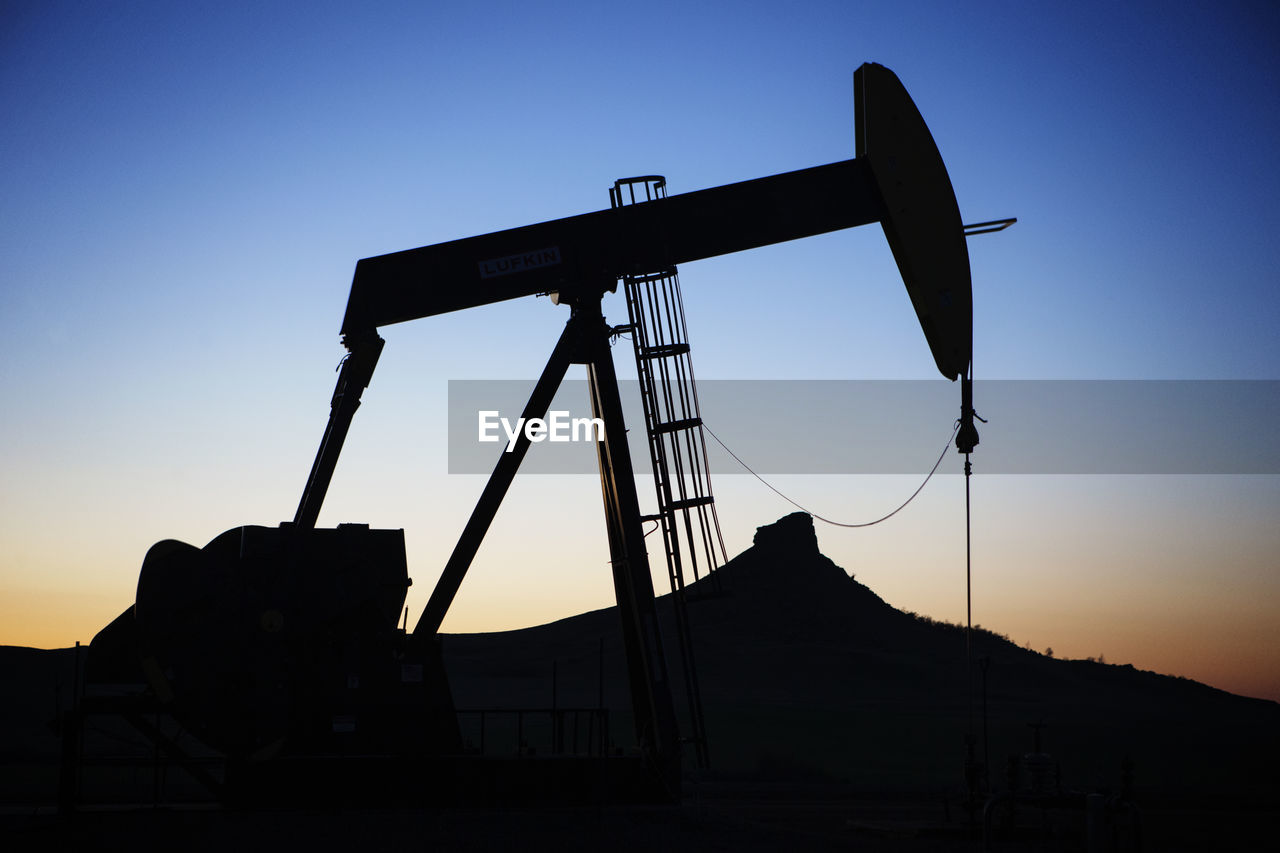 Silhouette oil pump on field against sky during sunset