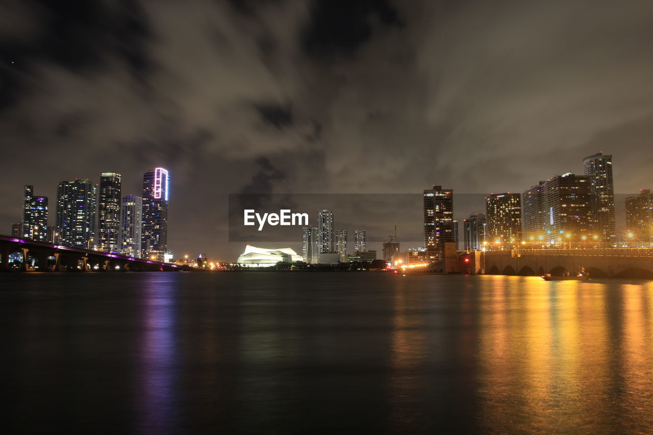 ILLUMINATED MODERN BUILDINGS BY SEA AGAINST SKY