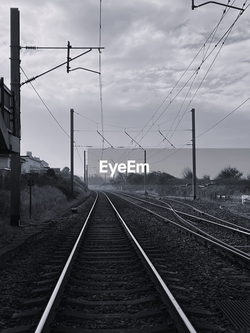 railroad track, track, rail transportation, cable, transportation, line, electricity, sky, transport, black and white, railway, electricity pylon, power line, cloud, technology, power supply, monochrome, nature, the way forward, mode of transportation, no people, vanishing point, monochrome photography, lane, diminishing perspective, architecture, overhead power line, vehicle, travel, outdoors, power generation, public transportation, wire, residential area, day, train station, parallel, built structure, railroad station, tree, sign