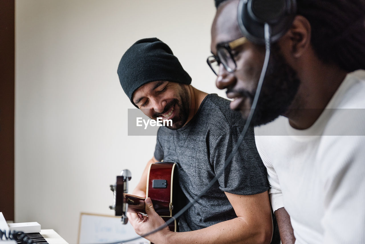 Man playing guitar while friend listening through headphones