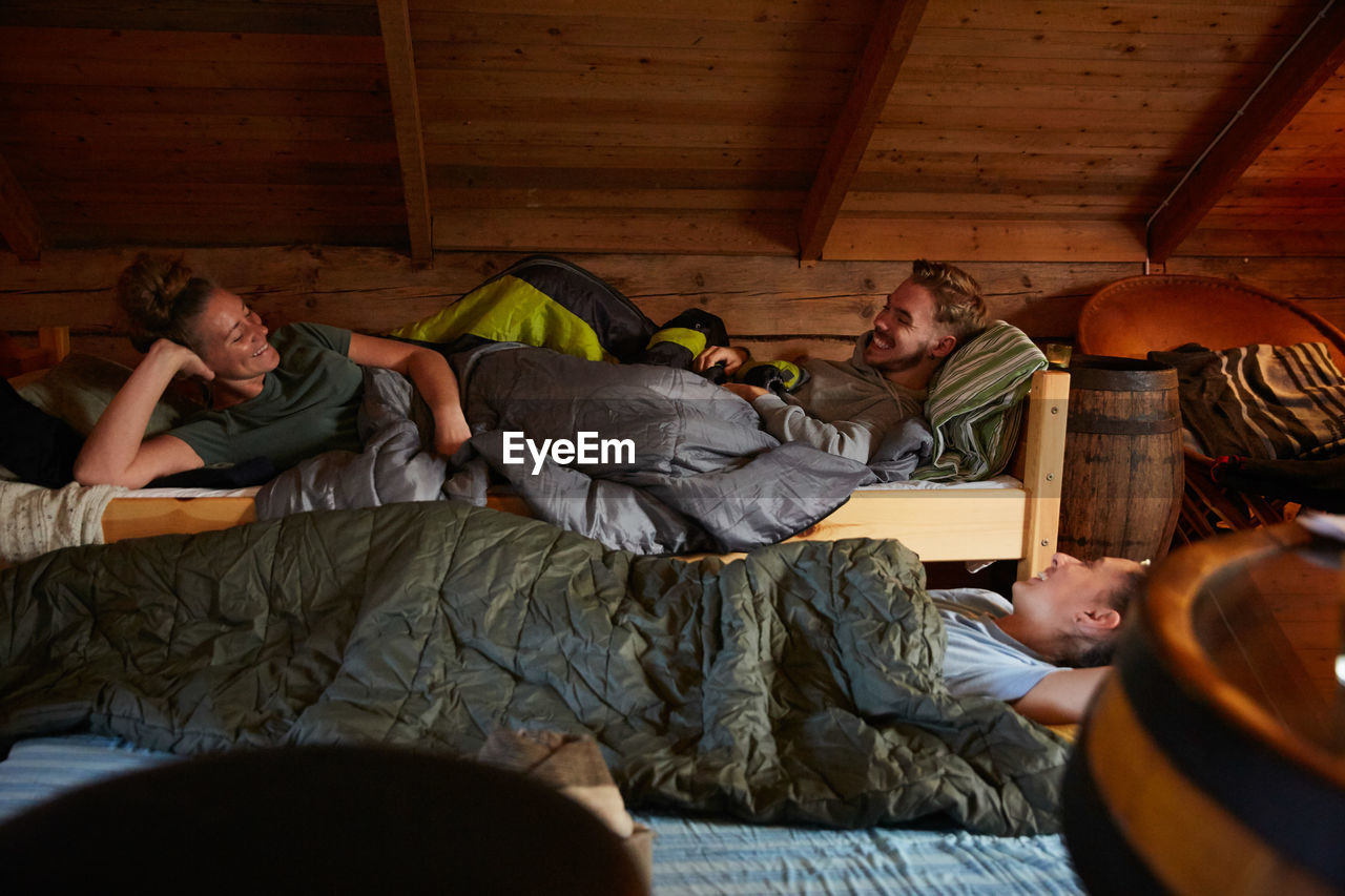 Smiling friends talking while resting in log cabin during bedtime