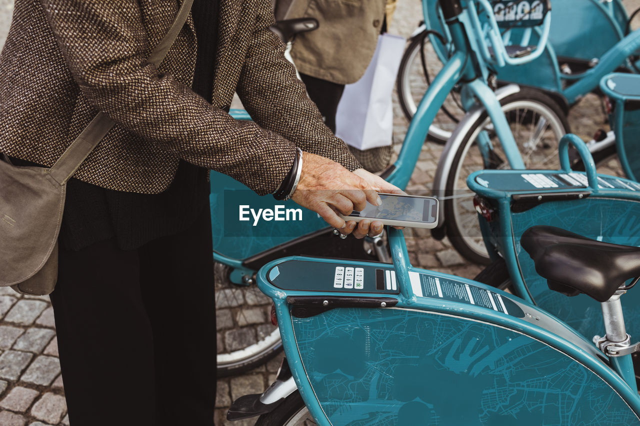 Midsection of senior woman scanning qr code of bicycle through smart phone at parking station