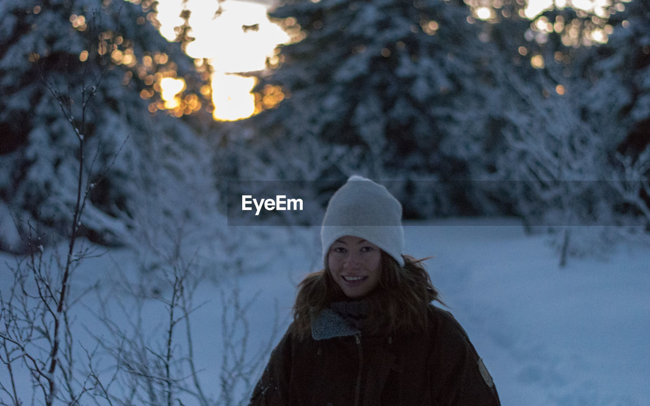 Portrait of smiling young woman standing in forest during winter