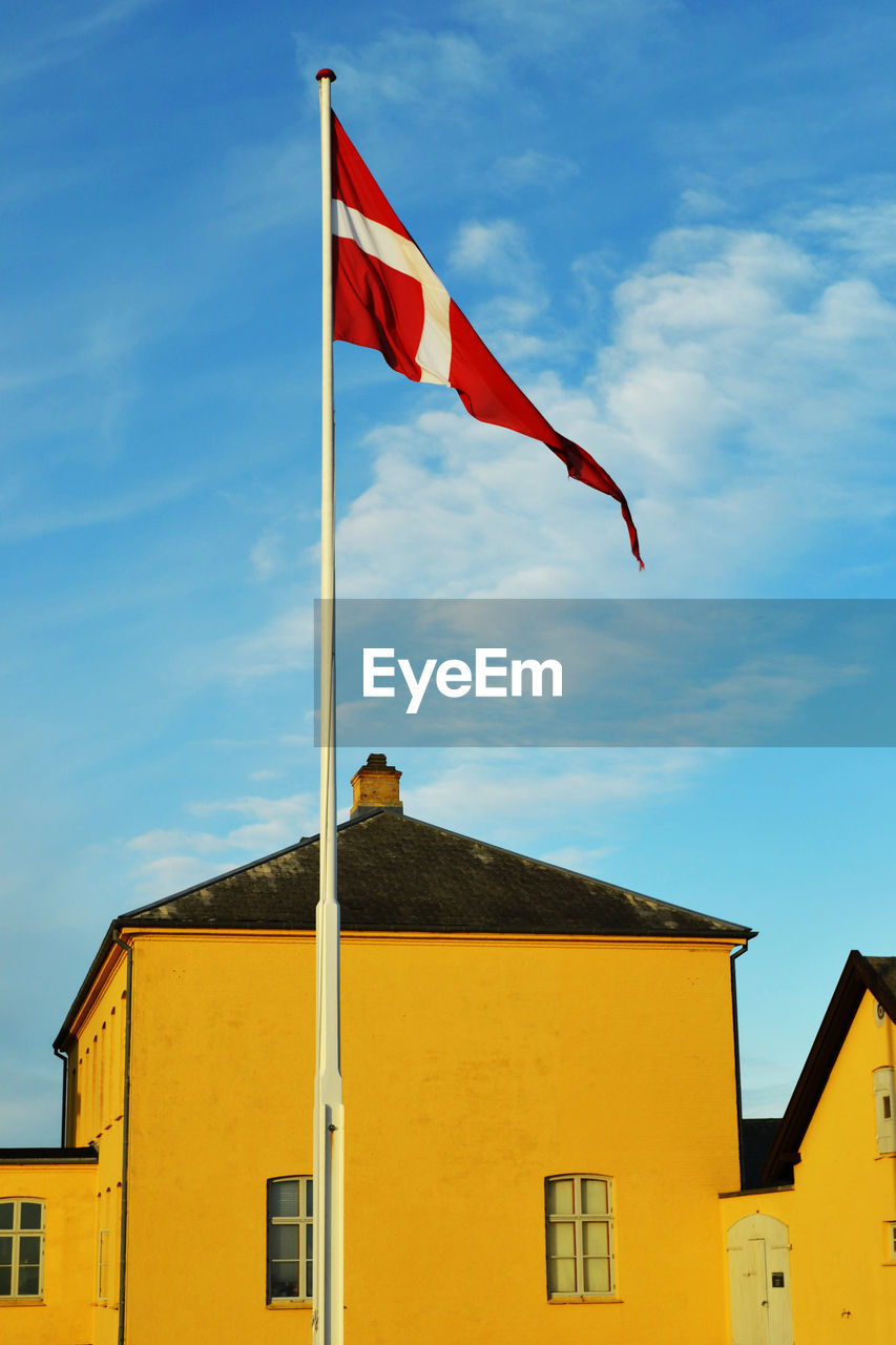 Low angle view of danish flag waving against yellow building