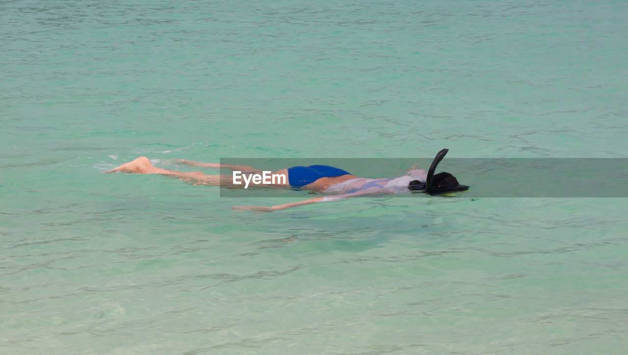 HIGH ANGLE VIEW OF MAN LYING IN SEA