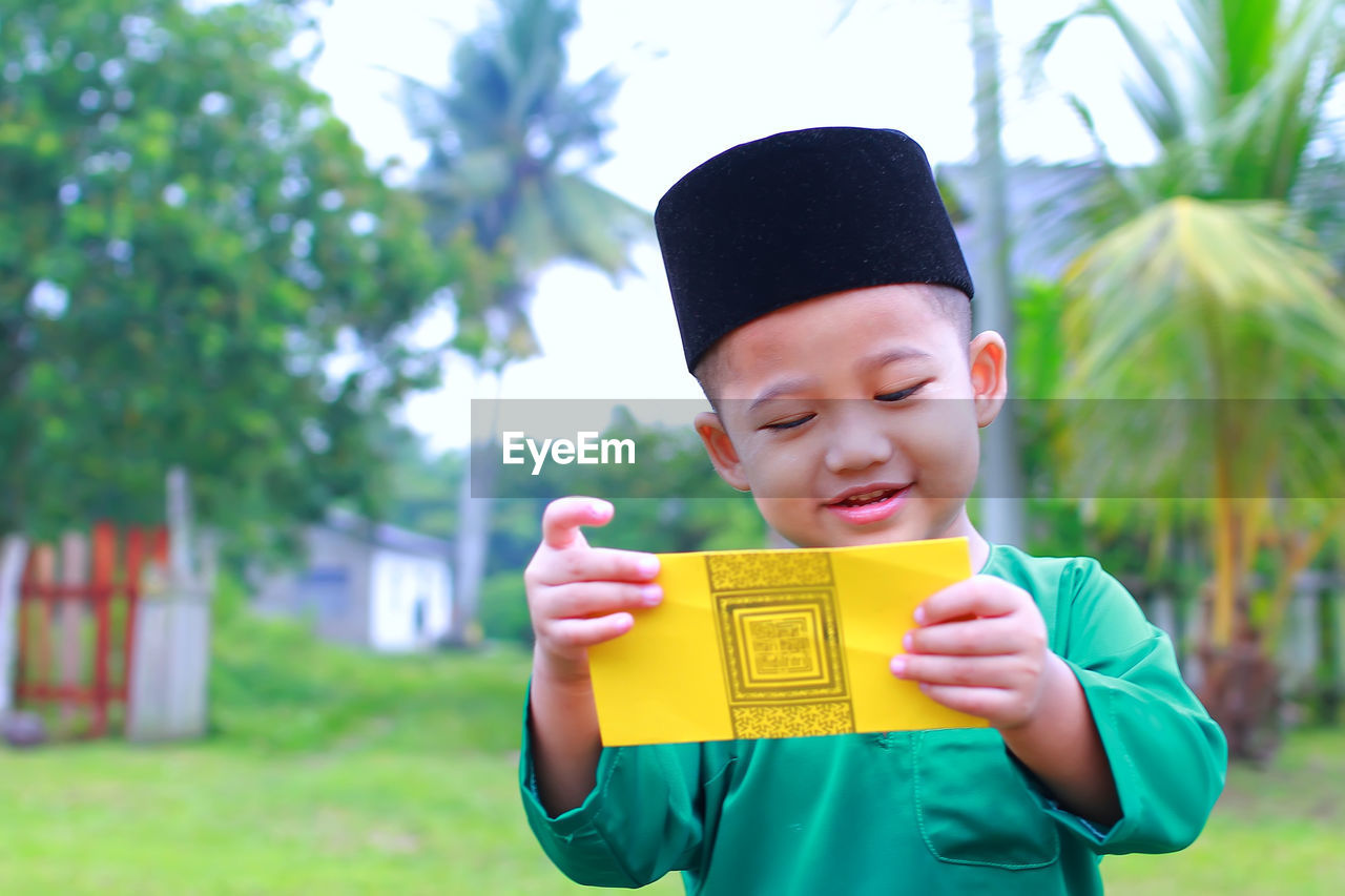 Boy in traditional clothing holding envelope while standing on field