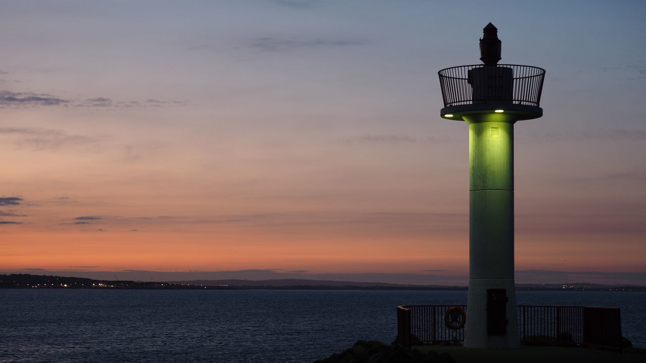 Scenic view of lighthouse by sea against sky during sunset