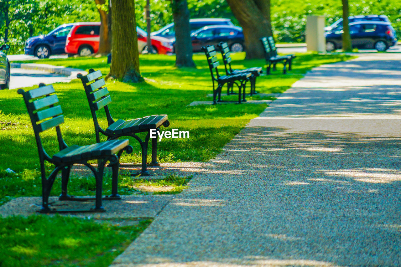 plant, park, seat, park - man made space, grass, lawn, tree, empty, green, nature, bench, park bench, transportation, day, absence, city, car, no people, public space, chair, shadow, sunlight, mode of transportation, relaxation, footpath, playground, outdoors, furniture, road, growth, recreation, tree trunk, trunk, street, tranquility, walkway, vehicle, the way forward, motor vehicle, land vehicle