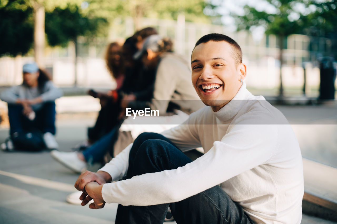 Portrait of happy young man sitting with friends at skateboard park