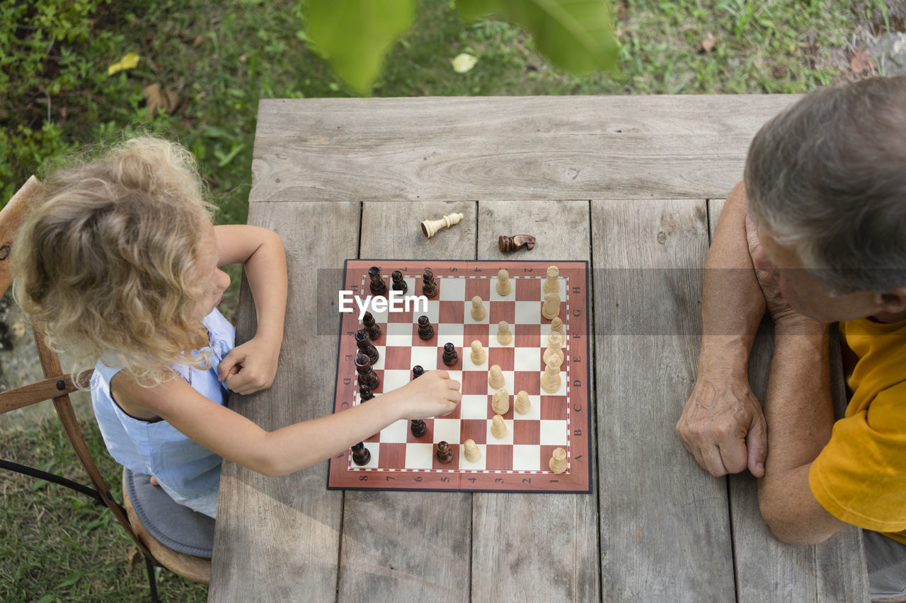 Granddaughter and grandfather playing chessboard in garden