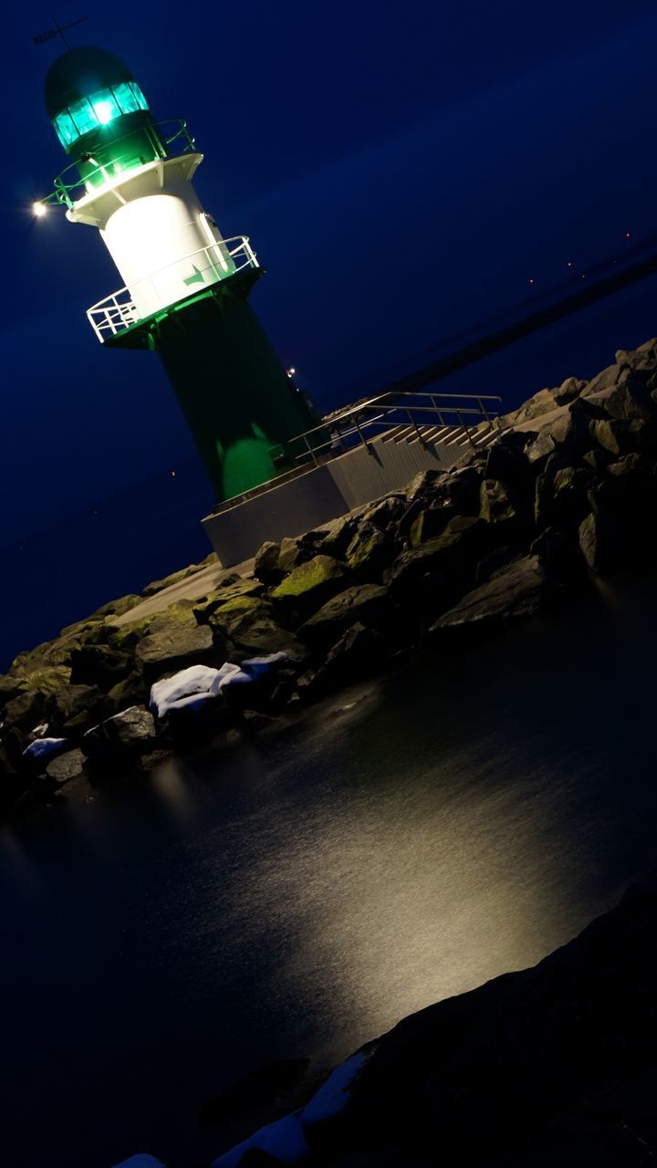 Low angle view of illuminated lighthouse by sea at night