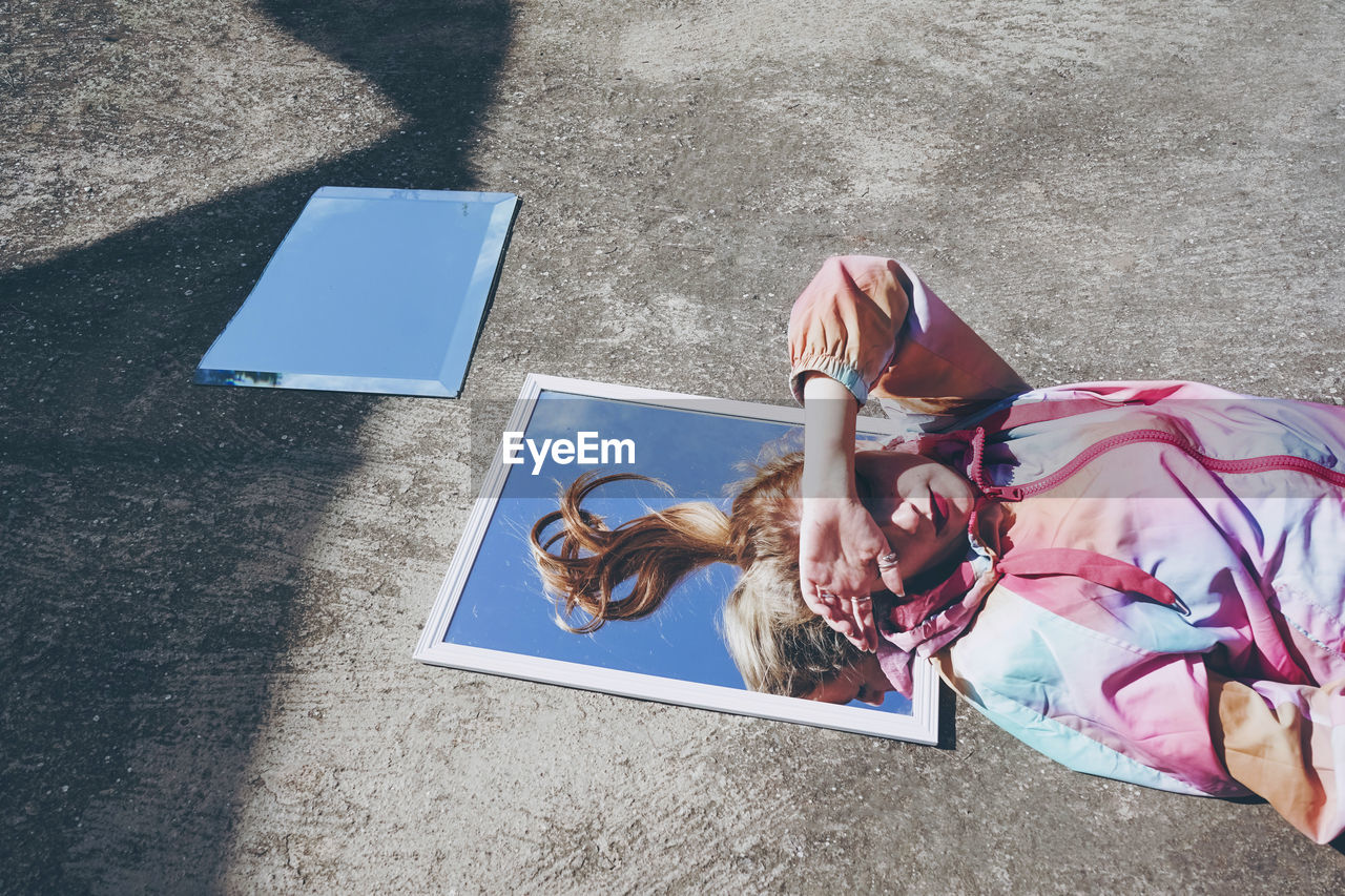 Woman shielding eyes from sunlight lying down on mirror