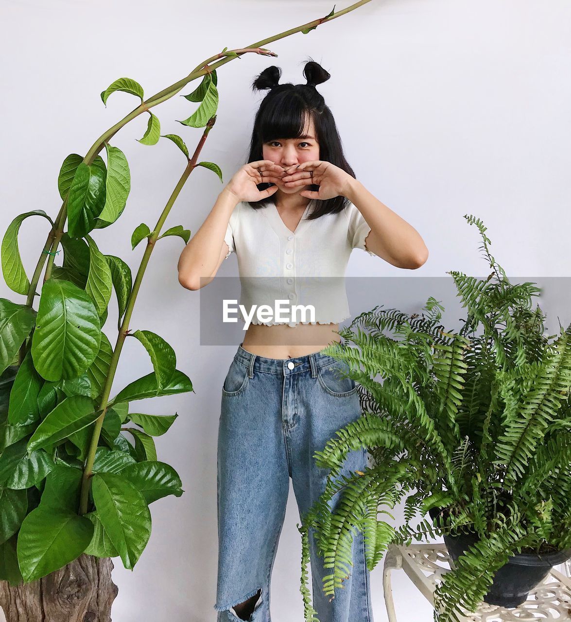 Portrait of young woman standing against plants over white background 