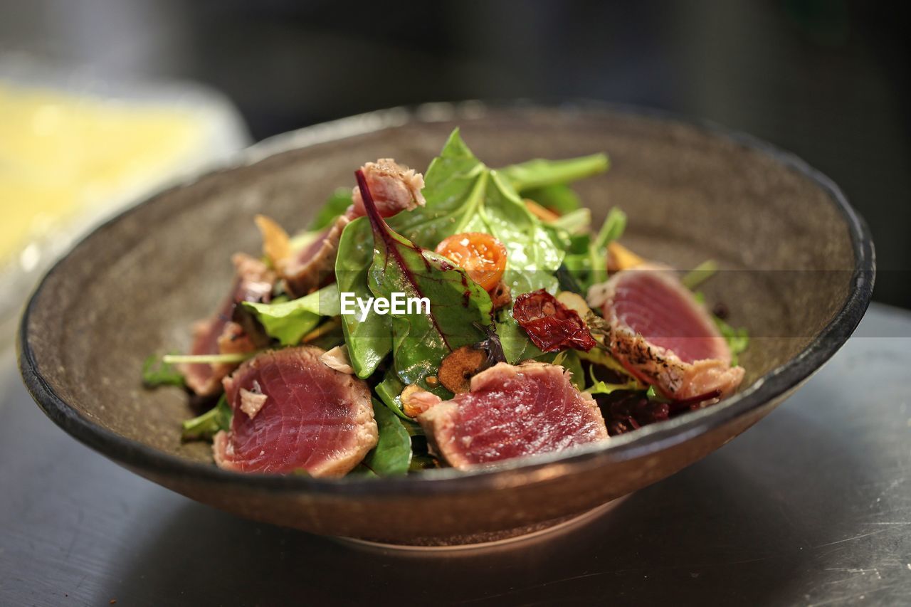 Close-up of tuna slices and leaves in bowl on table