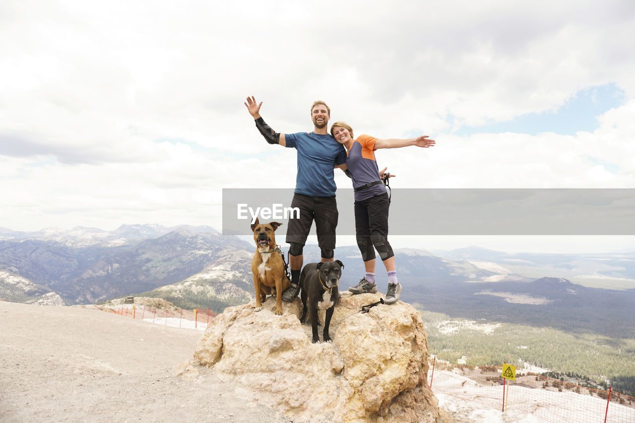 Portrait of couple with dogs standing on mountain against cloudy sky