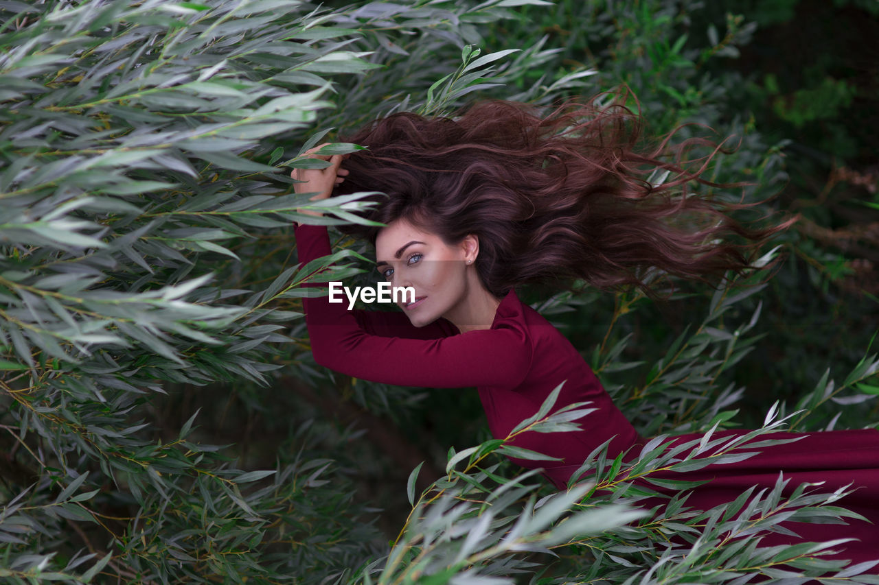 Portrait of young woman in maroon dress amidst shrubs