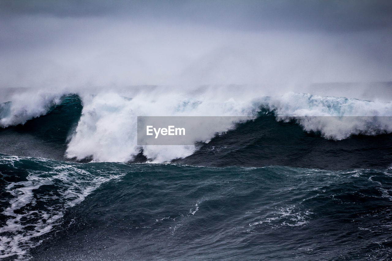 SCENIC VIEW OF WAVES SPLASHING ON SHORE AGAINST SKY