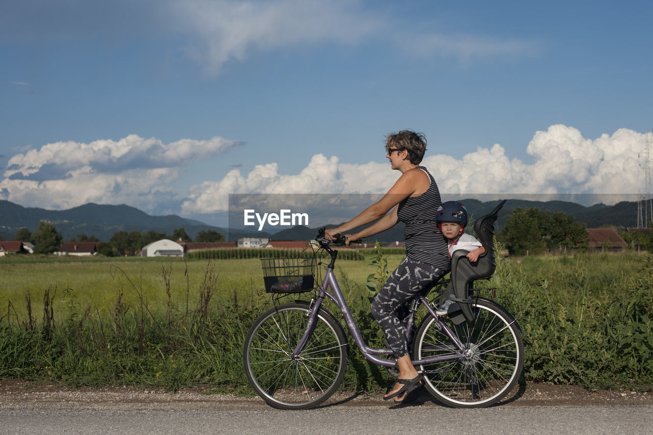 Mother with her son riding bicycle on field against sky