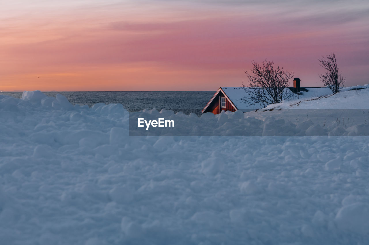 Snow covered land and sea against sky during sunset