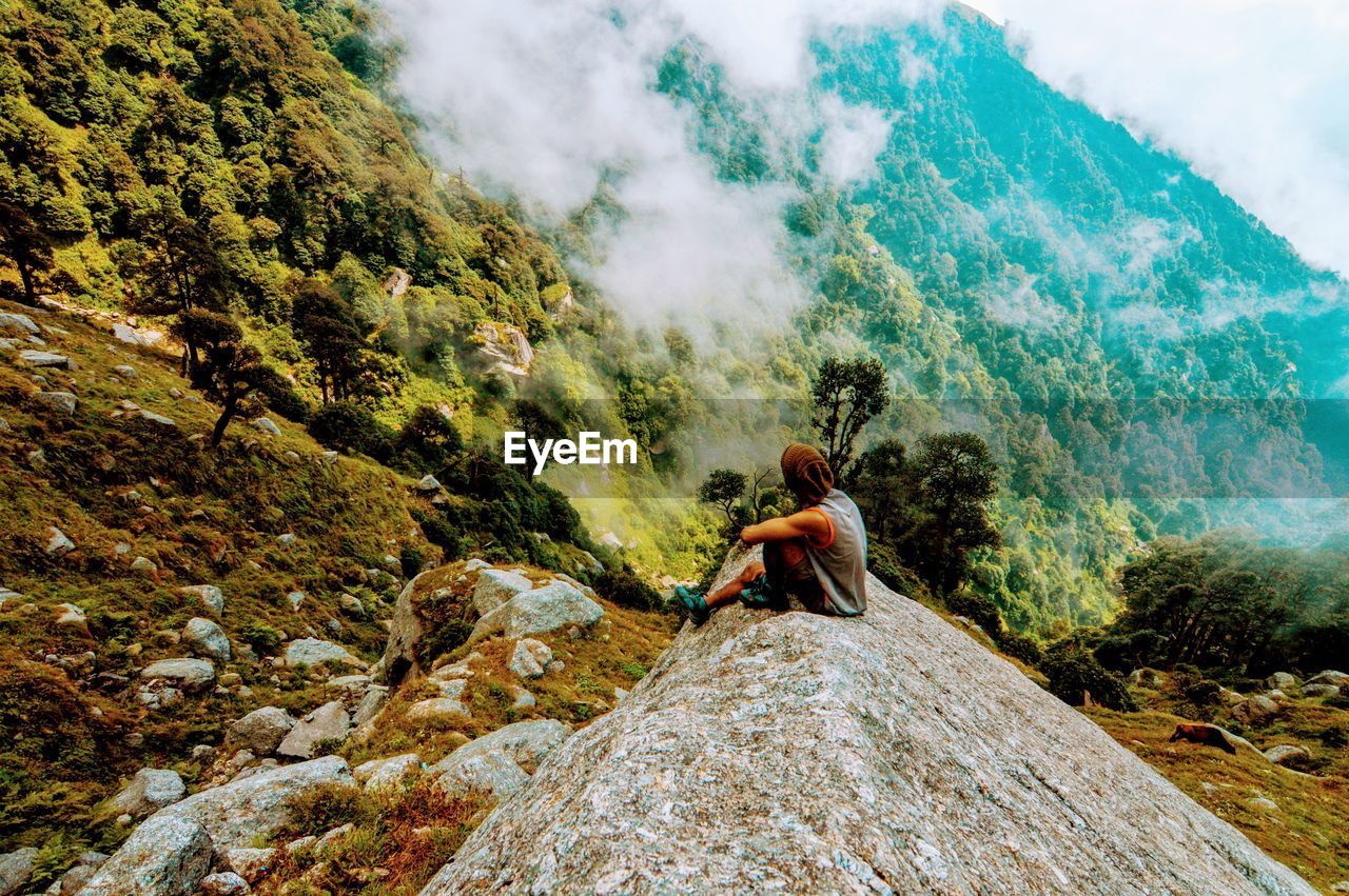 Young man sitting on rock by mountains